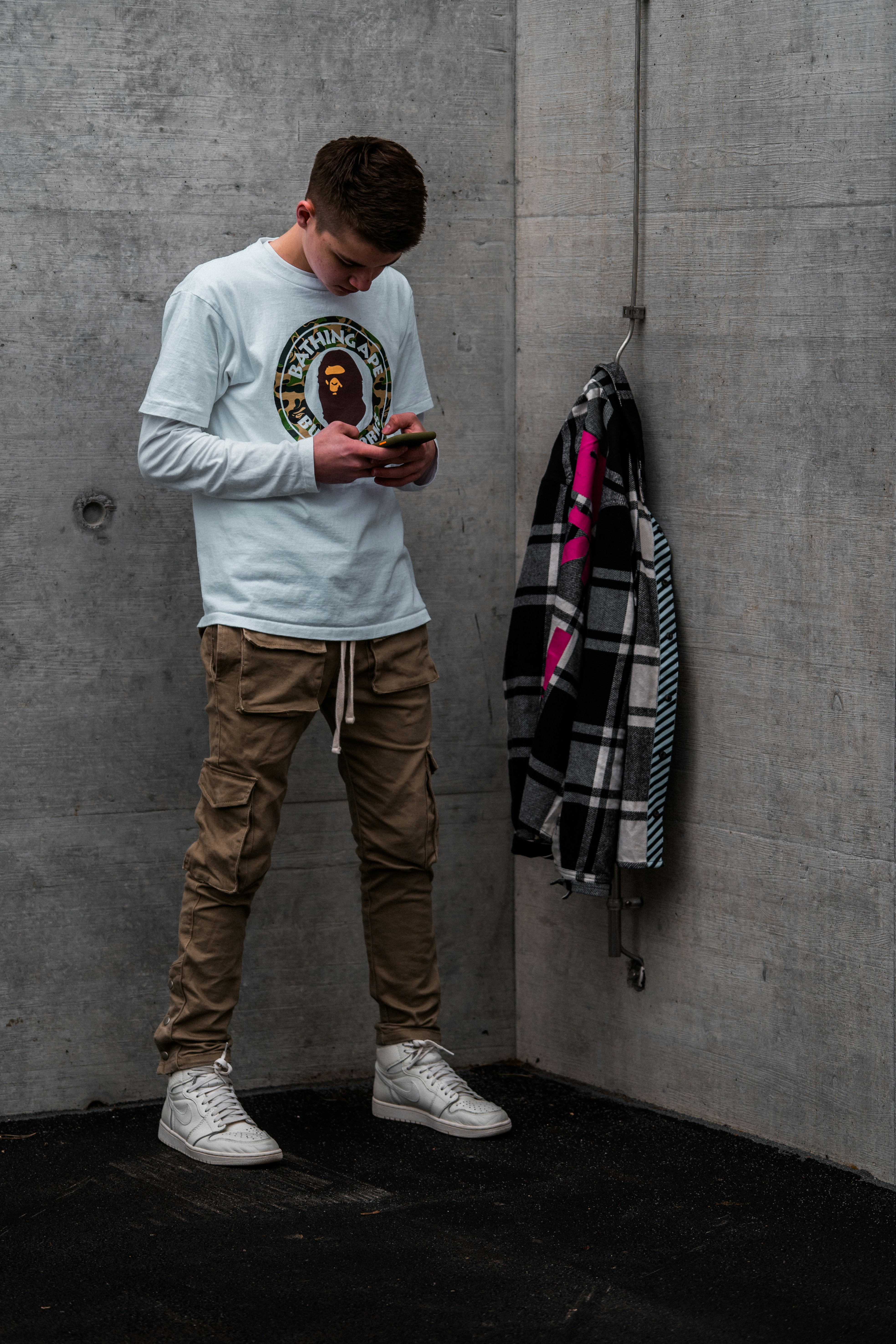 Black oversized tee hanging on concrete wall, underground editorial aesthetic with dim lighting