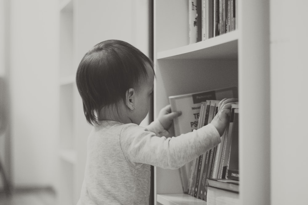 child in white long sleeve shirt standing beside white wooden shelf