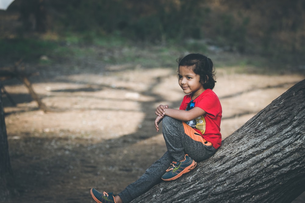 boy in red t-shirt and blue denim jeans sitting on wood log