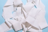 A tangled heap of white paper towel or tissue strips set against a light blue background. The paper appears textured and creates a complex pattern with folds and layers.