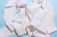 A tangled heap of white paper towel or tissue strips set against a light blue background. The paper appears textured and creates a complex pattern with folds and layers.