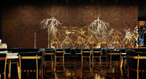 A luxurious and sophisticated interior space featuring elegant dining tables and chairs with black upholstery and wooden accents. The walls have a reflective, geometric design with intricate, illuminated floral decorations. The floor showcases a polished, patterned surface, contributing to the high-end atmosphere.