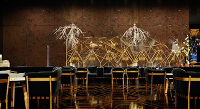 A luxurious and sophisticated interior space featuring elegant dining tables and chairs with black upholstery and wooden accents. The walls have a reflective, geometric design with intricate, illuminated floral decorations. The floor showcases a polished, patterned surface, contributing to the high-end atmosphere.