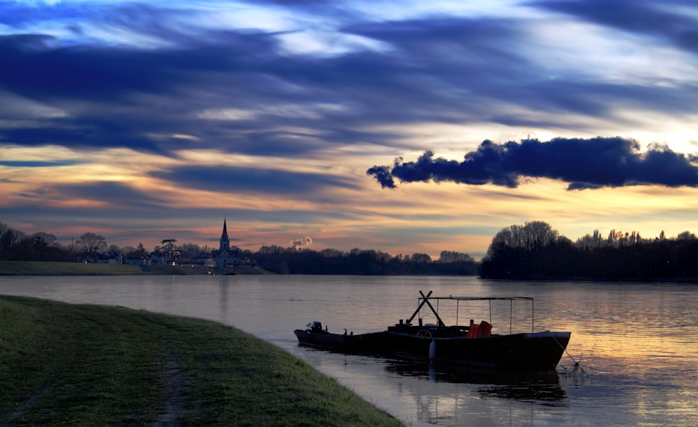 boat on water near green grass field during sunset