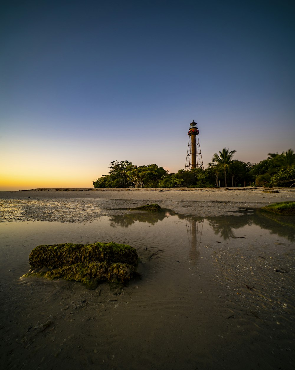 lighthouse on brown sand near body of water during sunset