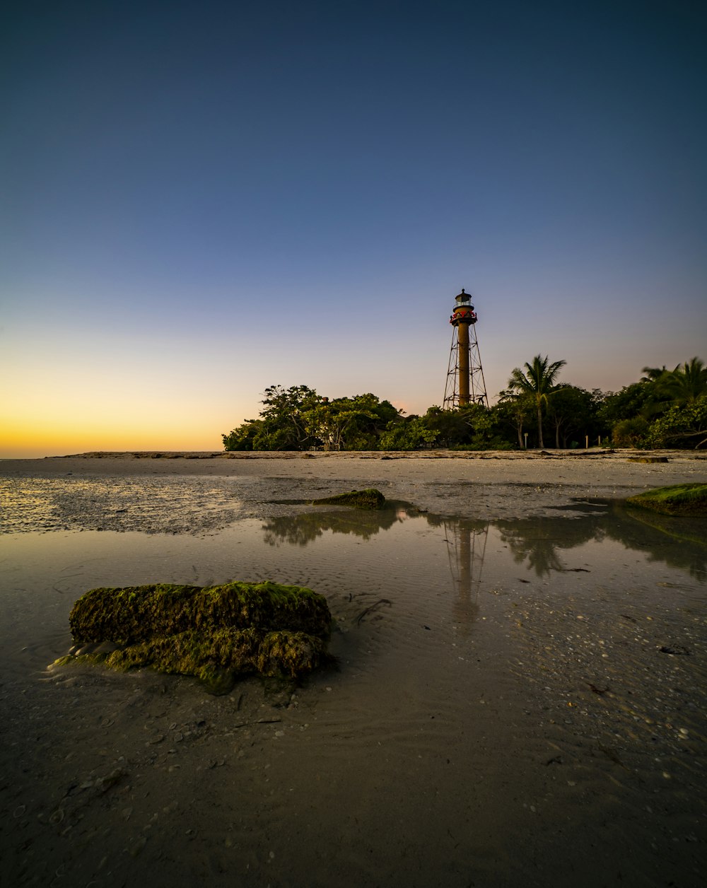 farol na areia marrom perto do corpo de água durante o pôr do sol