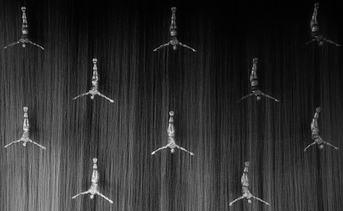 Several metallic human figures with outstretched arms and legs are arranged in an orderly pattern, resembling divers in a dynamic pose. Each figure is positioned against the textured background that resembles cascading water or strands of silk, creating a striking contrast between the smooth, reflective surfaces of the figures and the dark, flowing background.