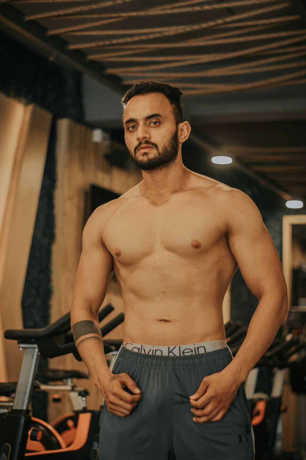 topless man in black shorts standing near brown wooden wall