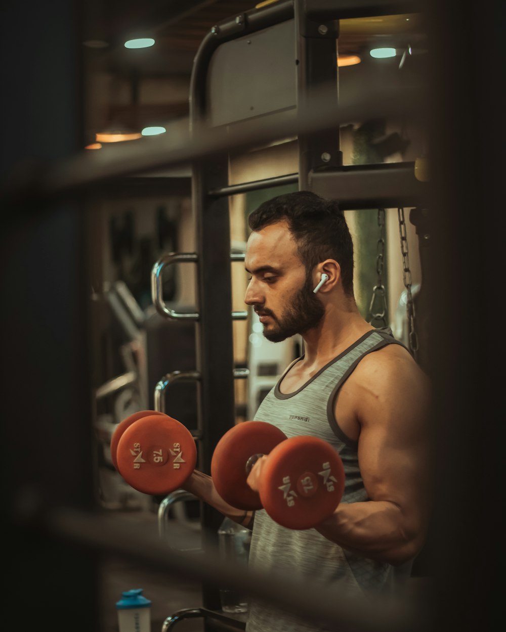 man in gray tank top holding red dumbbells