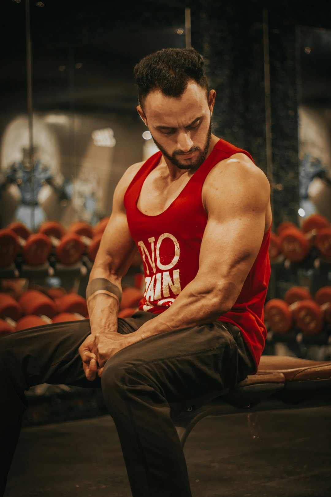 man in red tank top and black pants sitting on brown wooden bench