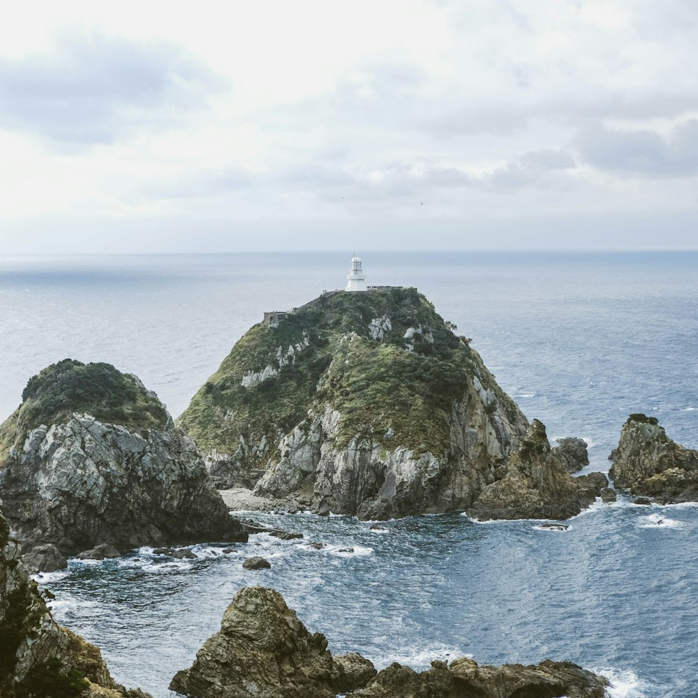 日中の水域近くの灰色の岩層の上にある白い灯台