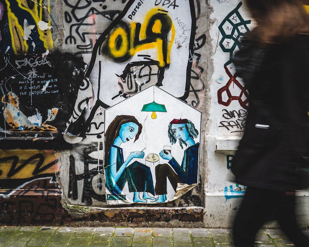 man in black jacket standing beside wall with graffiti