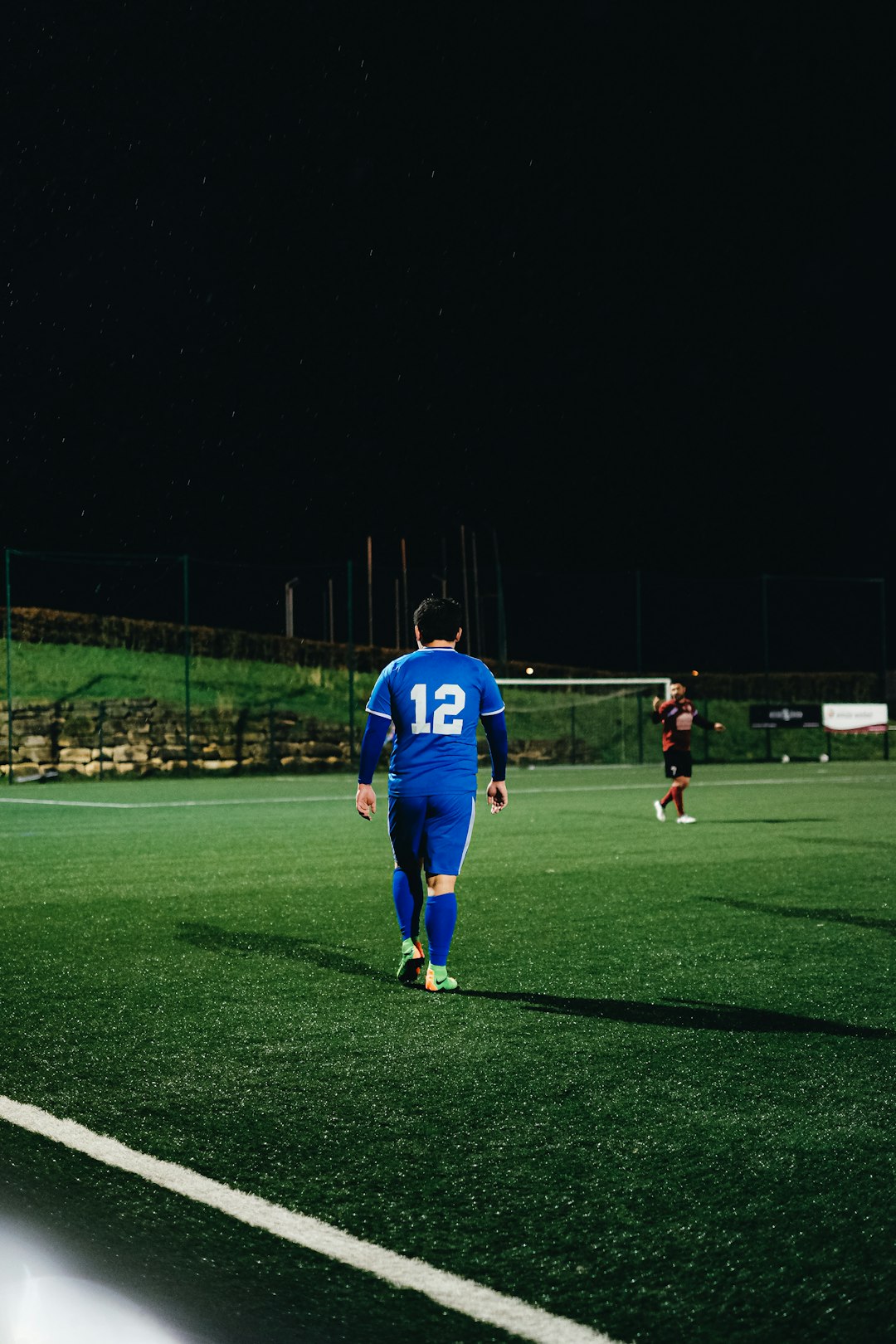 man in blue jersey shirt and black shorts standing on green grass field during nighttime