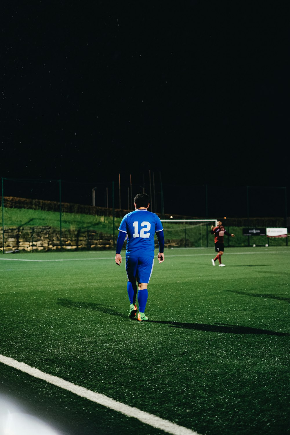 uomo in maglia blu camicia e pantaloncini neri in piedi sul campo in erba verde durante la notte