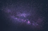 A serene view of Earth from space with stars and distant galaxies in purple and pink tones.