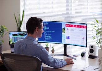 man in gray dress shirt sitting on chair in front of computer monitor