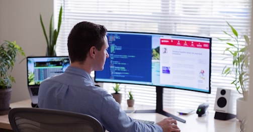 man in gray dress shirt sitting on chair in front of computer monitor