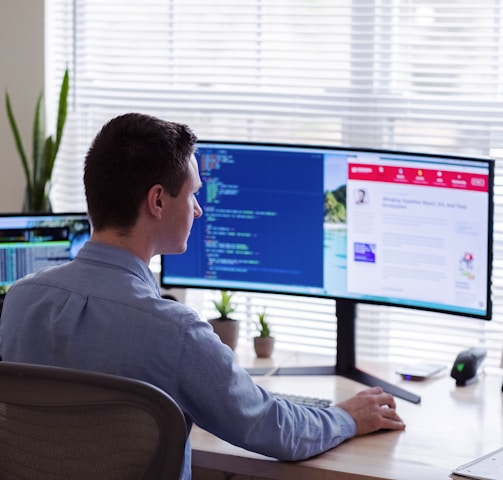 man in gray dress shirt sitting on chair in front of computer monitor