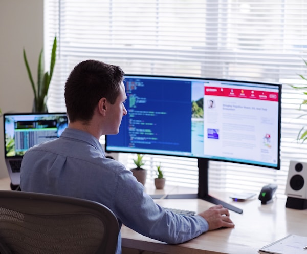 man in gray dress shirt sitting on chair in front of computer monitor