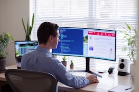 man in gray dress shirt sitting on chair in front of computer monitor