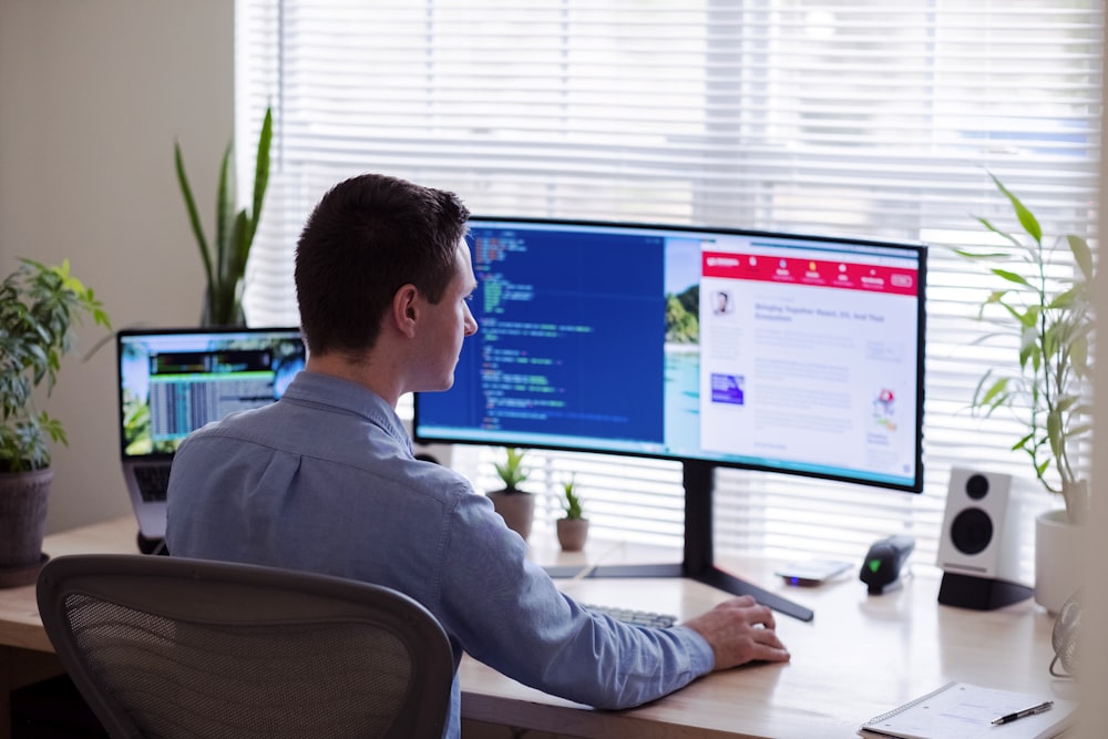 homem na camisa social cinza sentado na cadeira na frente do monitor do computador