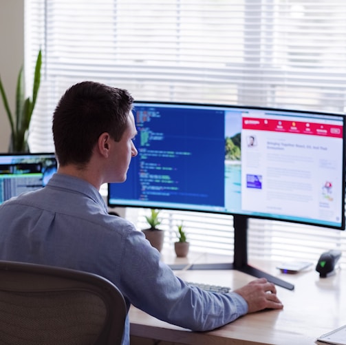 man in gray dress shirt sitting on chair in front of computer monitor