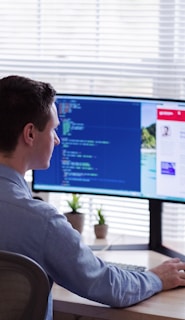 man in gray dress shirt sitting on chair in front of computer monitor