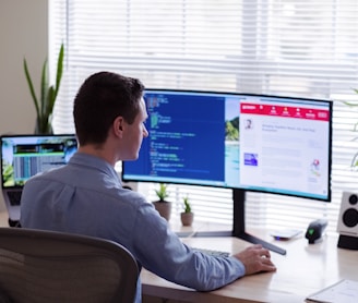 man in gray dress shirt sitting on chair in front of computer monitor