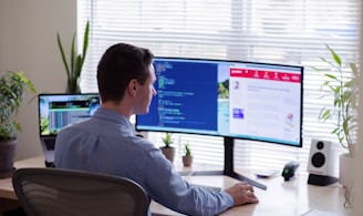 man in gray dress shirt sitting on chair in front of computer monitor