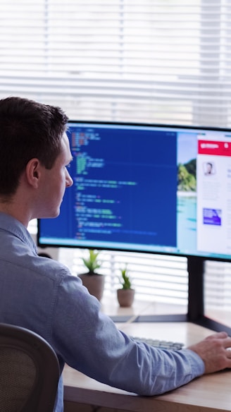 man in gray dress shirt sitting on chair in front of computer monitor