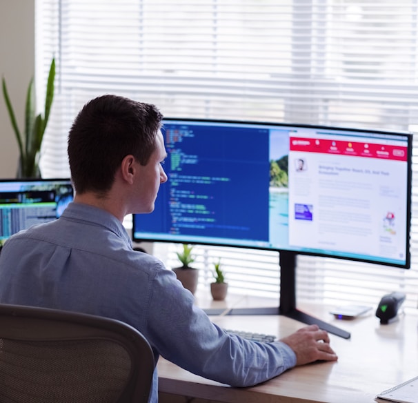 man in gray dress shirt sitting on chair in front of computer monitor