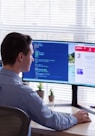 man in gray dress shirt sitting on chair in front of computer monitor