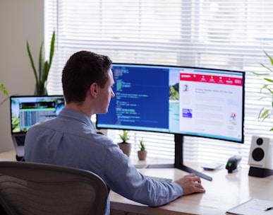 man in gray dress shirt sitting on chair in front of computer monitor