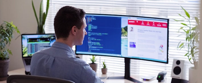 man in gray dress shirt sitting on chair in front of computer monitor