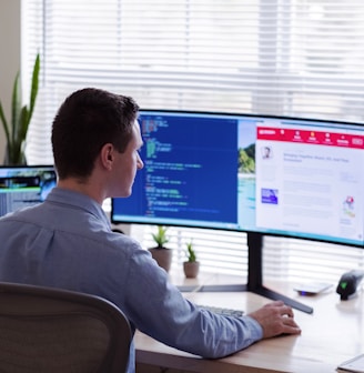 man in gray dress shirt sitting on chair in front of computer monitor