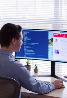 man in gray dress shirt sitting on chair in front of computer monitor