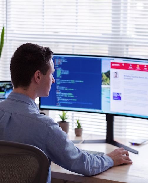 man in gray dress shirt sitting on chair in front of computer monitor