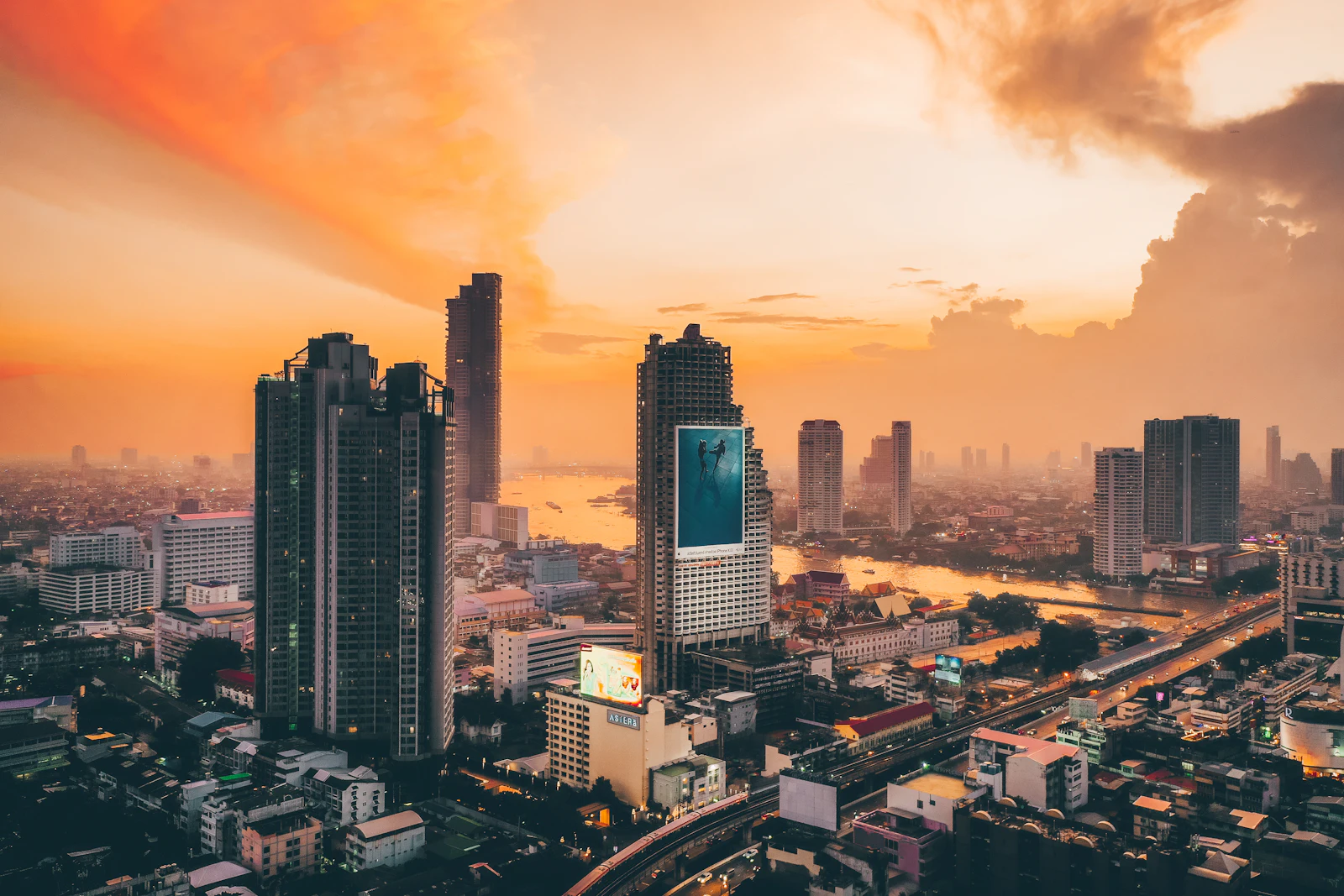 Bangkok high-rise skyline and the Chao Phraya River under an orange sunset sky, a city best explored with a Bangkok eSIM