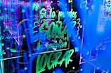 Bright neon lights create an energetic and lively atmosphere with glowing text and decorative symbols filling the space. The text, in Spanish, conveys an inspirational message amidst a backdrop of stars and abstract patterns.