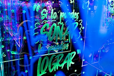 Bright neon lights create an energetic and lively atmosphere with glowing text and decorative symbols filling the space. The text, in Spanish, conveys an inspirational message amidst a backdrop of stars and abstract patterns.