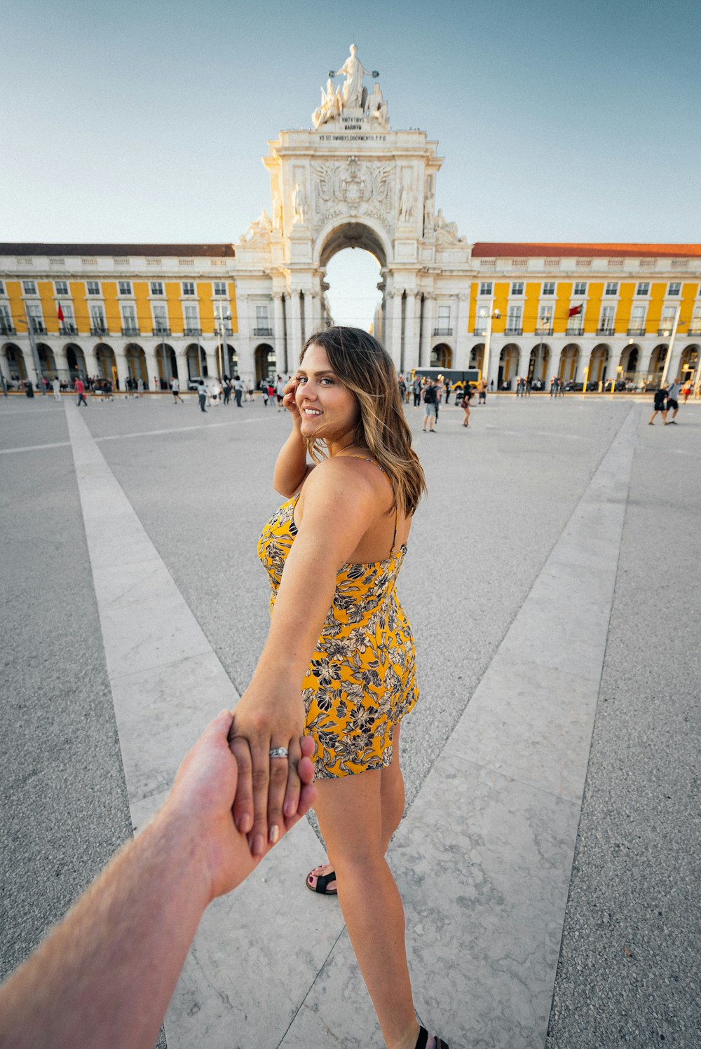 Mujer con vestido de tirantes de espagueti floral azul y amarillo de pie sobre el suelo de hormigón gris durante el día