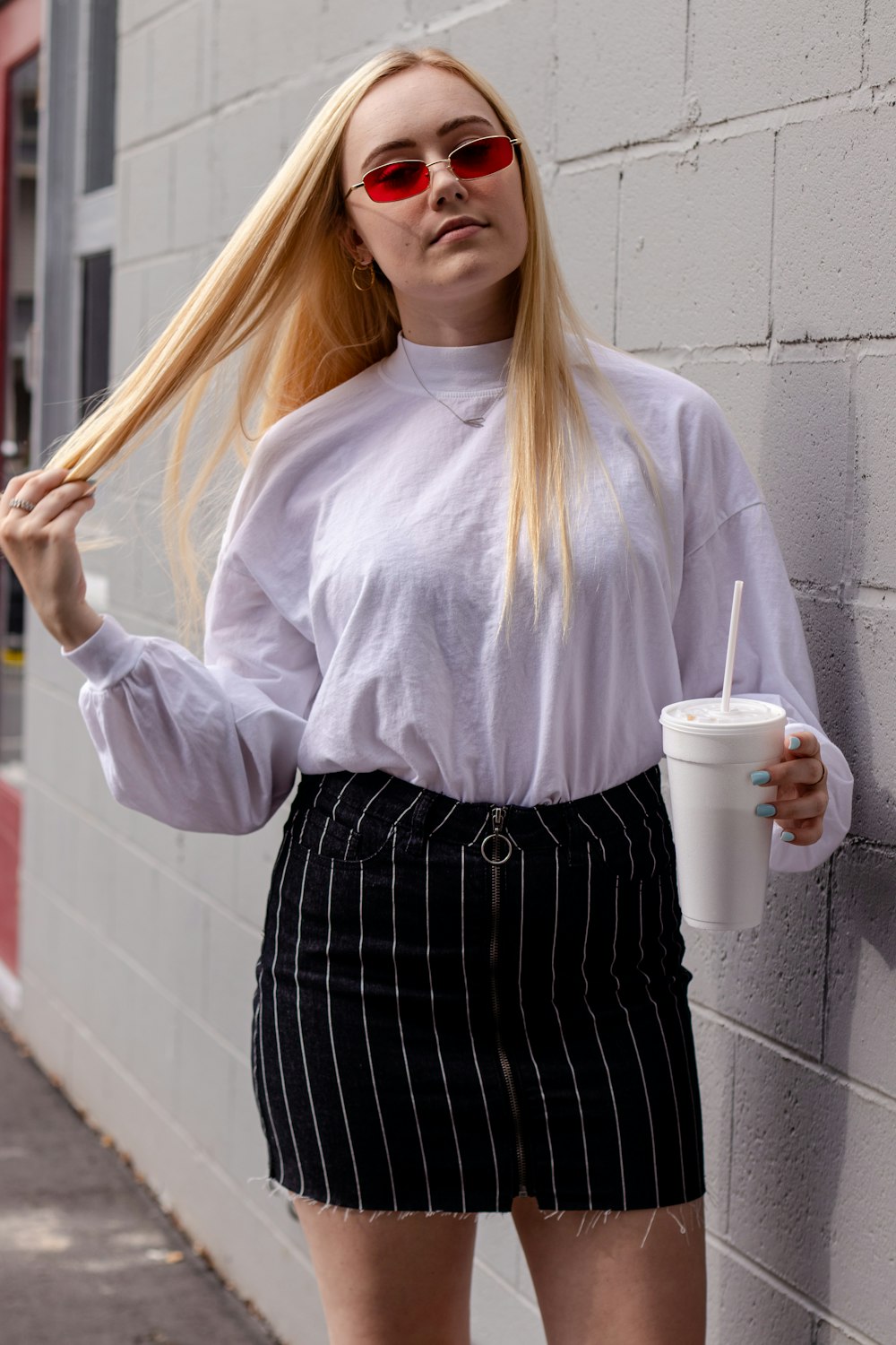 woman in white long sleeve shirt and black and white striped skirt holding white disposable cup