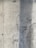 A textured concrete wall with visible signs of wear and a vertical shadow cast across part of its surface. The wall displays a rough texture with small holes and marks from the construction process.