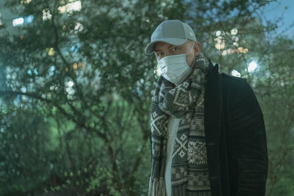 Homme en veste noire et casquette blanche debout près d’arbres verts pendant la journée