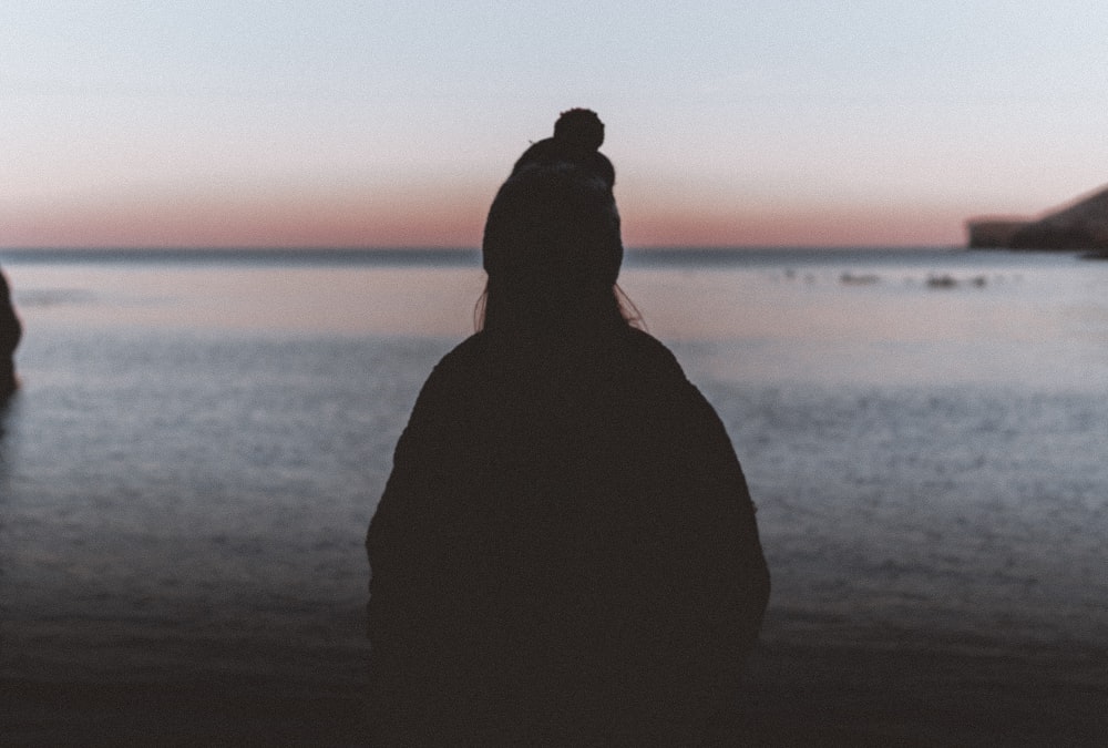 silhouette of person standing on seashore during sunset