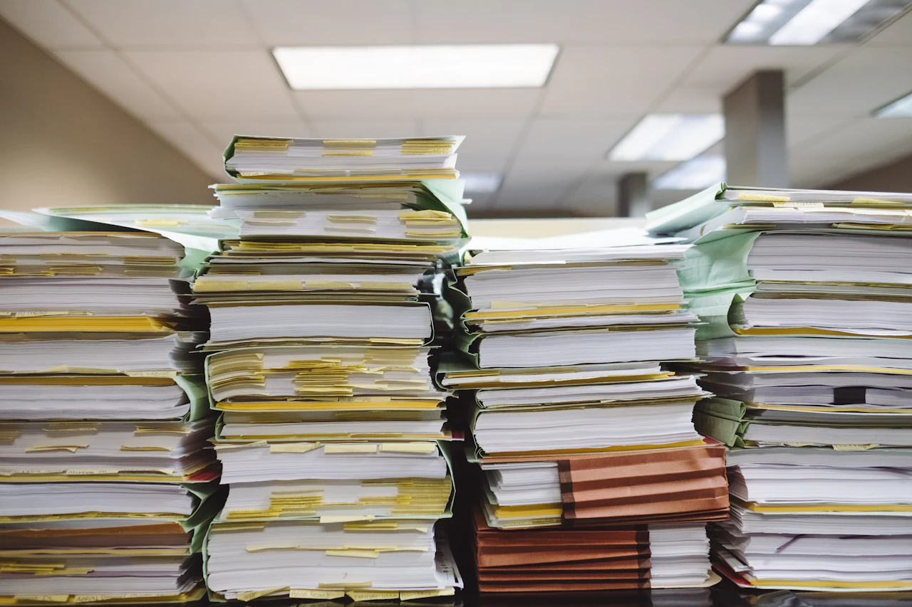 Stacks of paper files and folders representing the manual recordkeeping burden that automated compliance systems replace