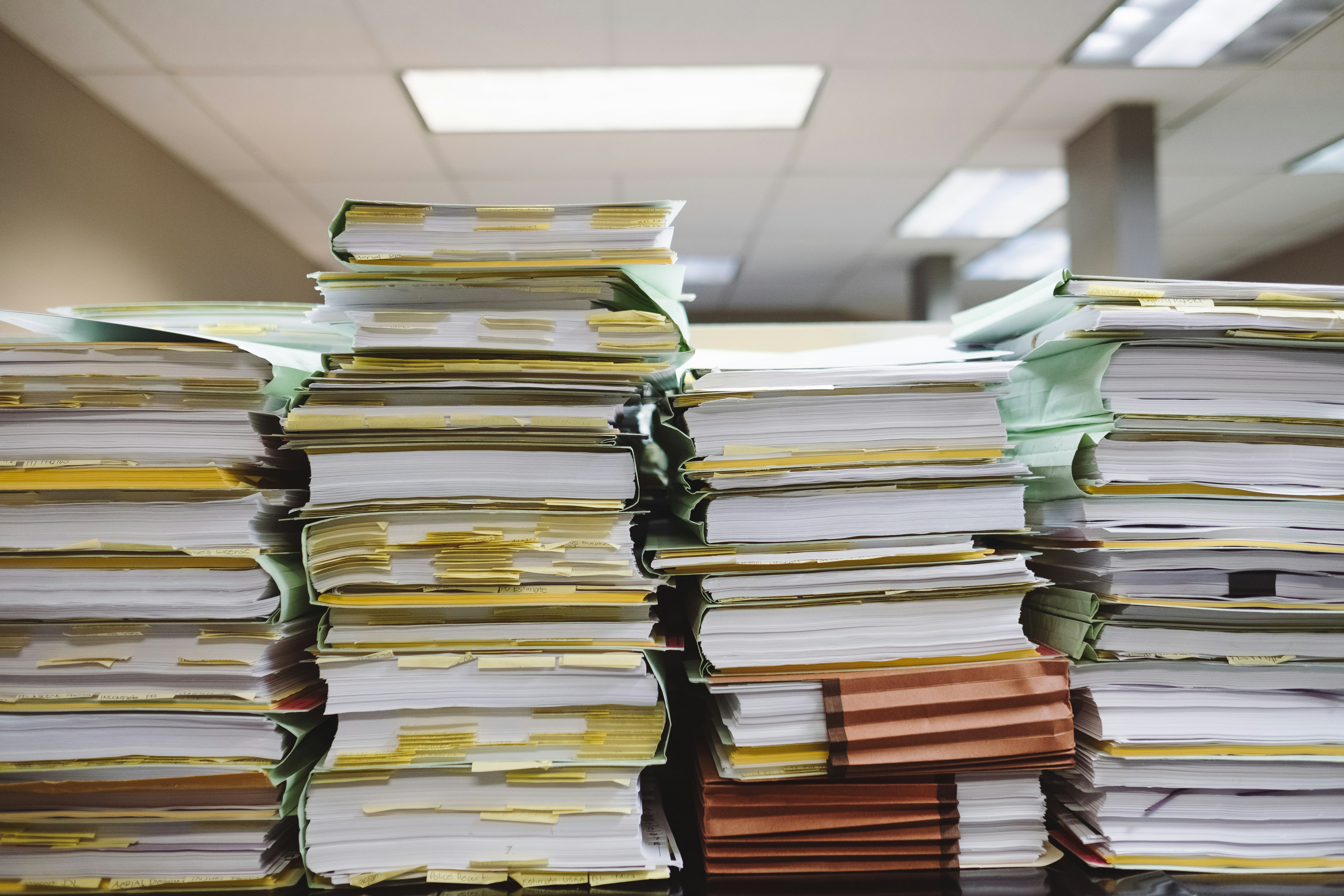 Image of paper stacked in files with yellow notes. <Photo by Wesley Tingey on Unsplash. 