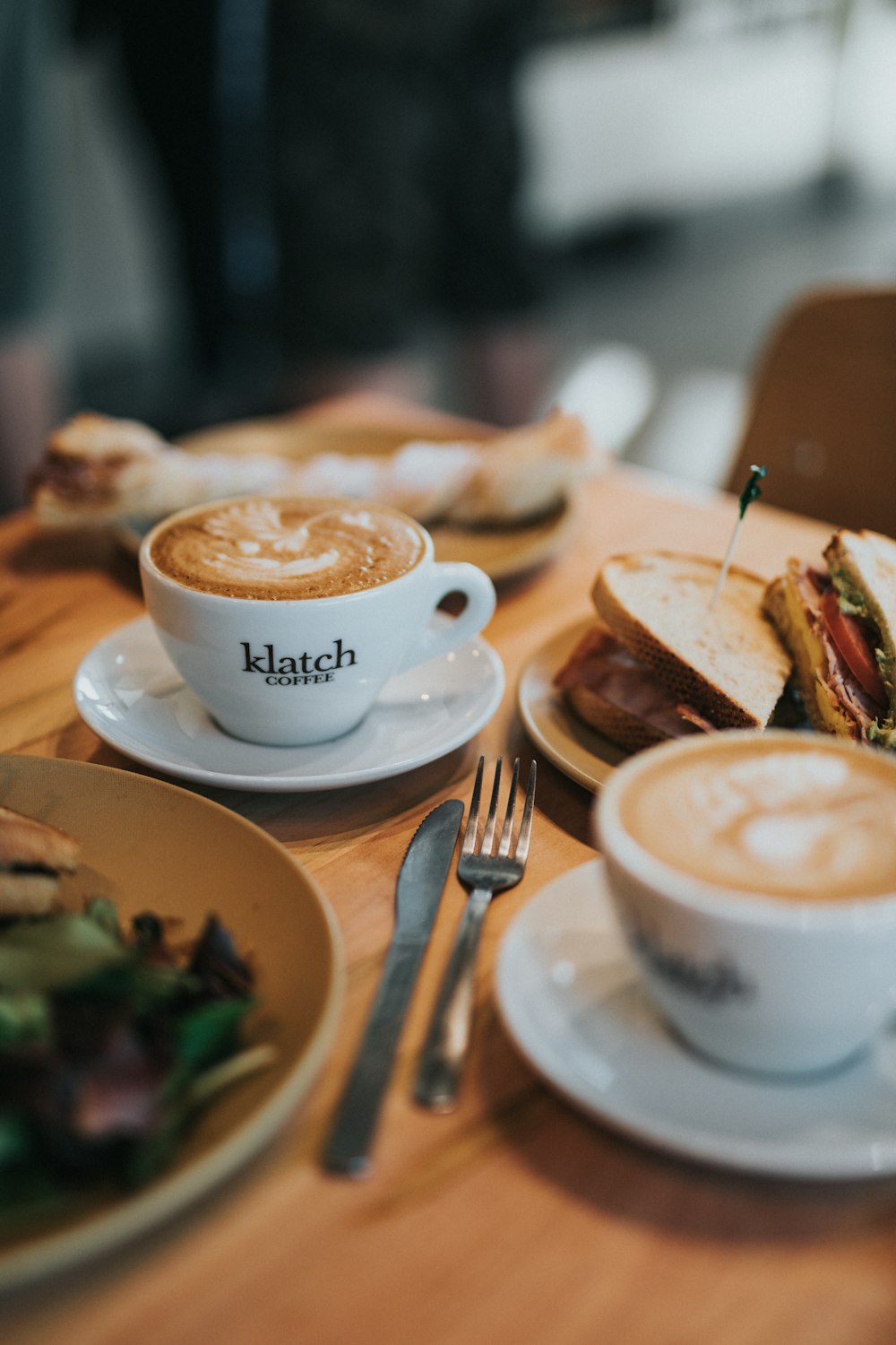 white ceramic cup with saucer beside stainless steel fork and bread knife