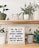 A close-up of colorful potted plants with motivational quote tags displayed on a wooden shelf.