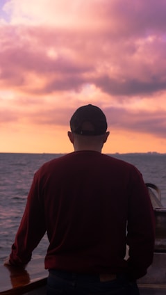 A confident captain standing on the deck of a sleek fishing boat, ocean horizon glowing with sunset hues behind him.